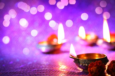 Image of Diwali celebration. Diya lamps and beautiful flowers on color background, closeup. Space for text. Bokeh effect