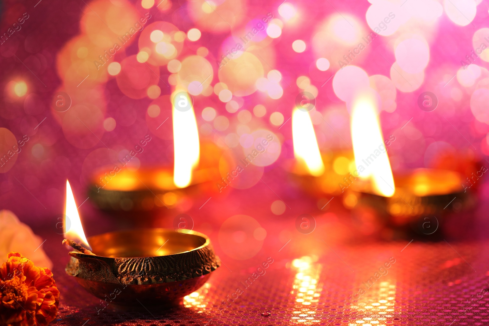 Image of Diwali celebration. Diya lamps and beautiful flowers on color background, closeup. Space for text. Bokeh effect