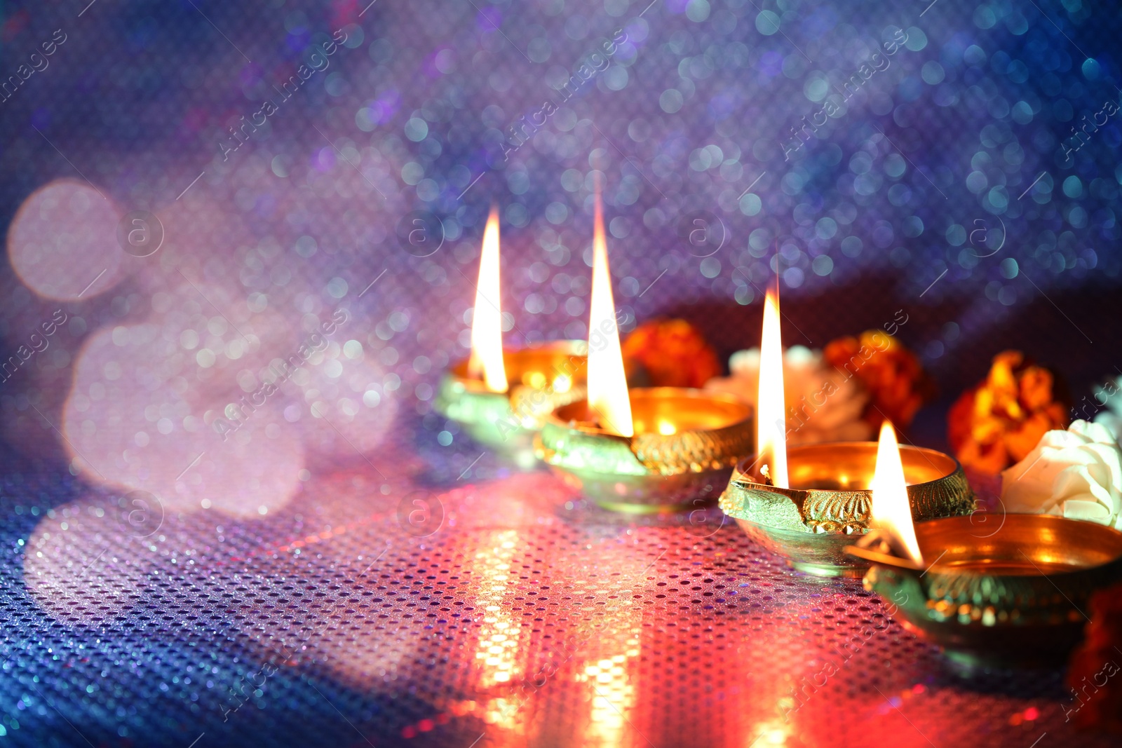 Image of Diwali celebration. Diya lamps and beautiful flowers on color background, closeup. Space for text. Bokeh effect