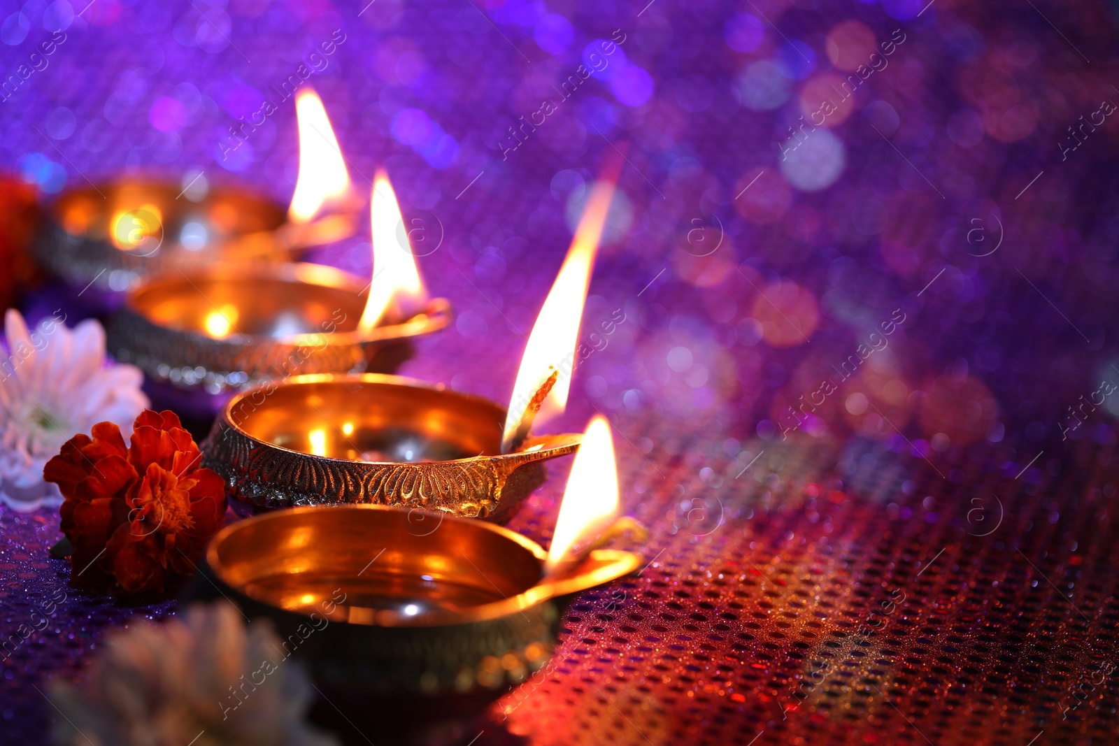 Image of Diwali celebration. Diya lamps and beautiful flowers on color background, closeup. Space for text. Bokeh effect