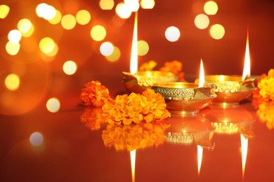 Image of Diwali celebration. Diya lamps and beautiful flowers on orange background, closeup. Bokeh effect