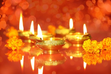 Image of Diwali celebration. Diya lamps and beautiful flowers on color background, closeup. Bokeh effect