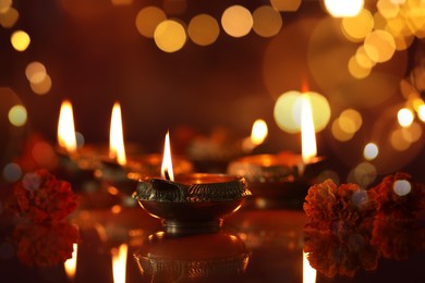 Image of Diwali celebration. Diya lamps and beautiful flowers on dark background, closeup. Bokeh effect