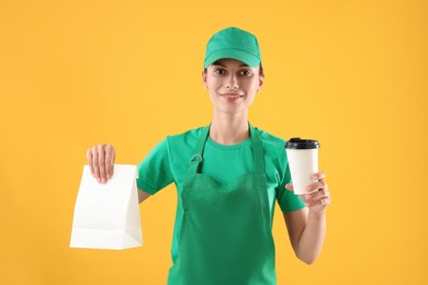 Photo of Fast-food worker with paper bag and cup on orange background