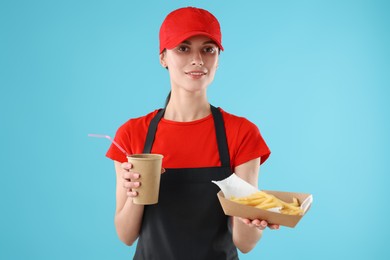 Photo of Fast-food worker with paper cup and fries on light blue background