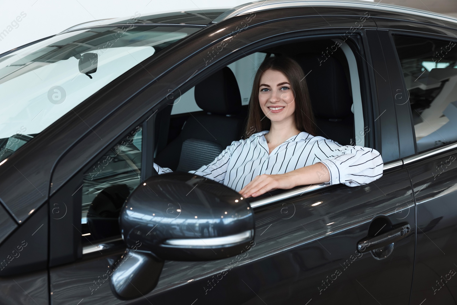 Photo of Happy young woman inside new car in salon