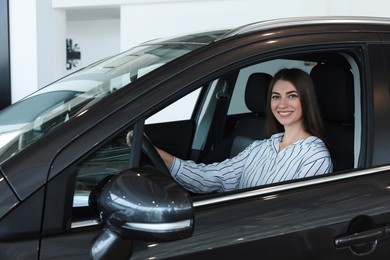 Happy young woman inside new car in salon