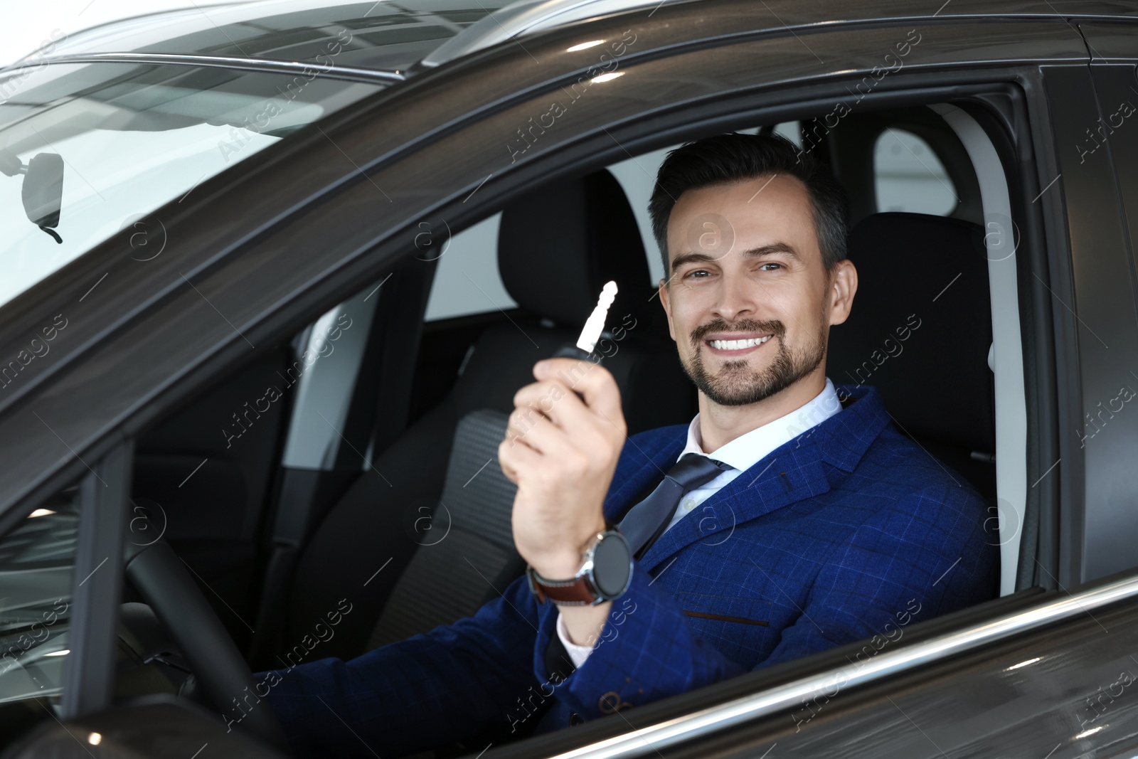 Photo of Happy salesman holding key inside new black car in salon