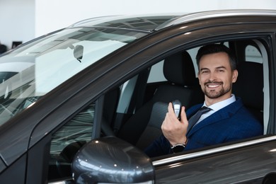 Photo of Happy salesman holding key inside new black car in salon