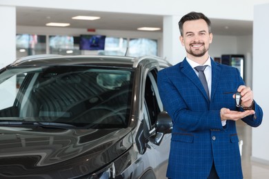 Photo of Happy salesman holding key near new black car in salon