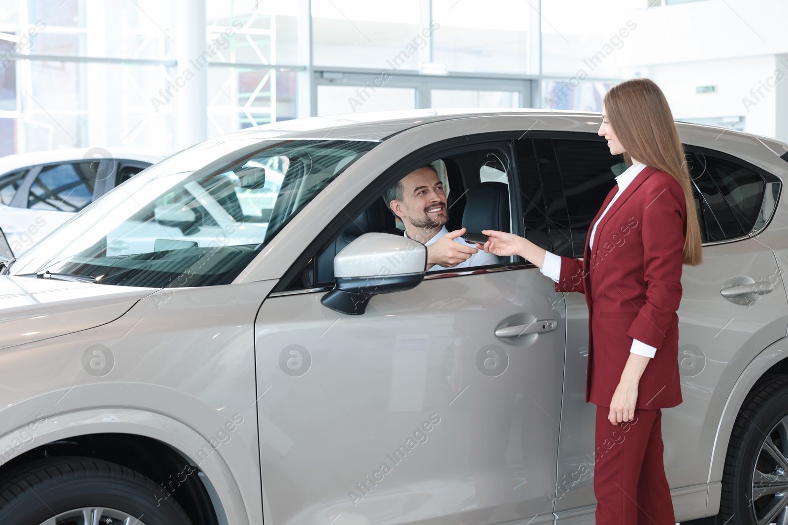 Photo of Happy saleswoman and client inside new silver car in salon