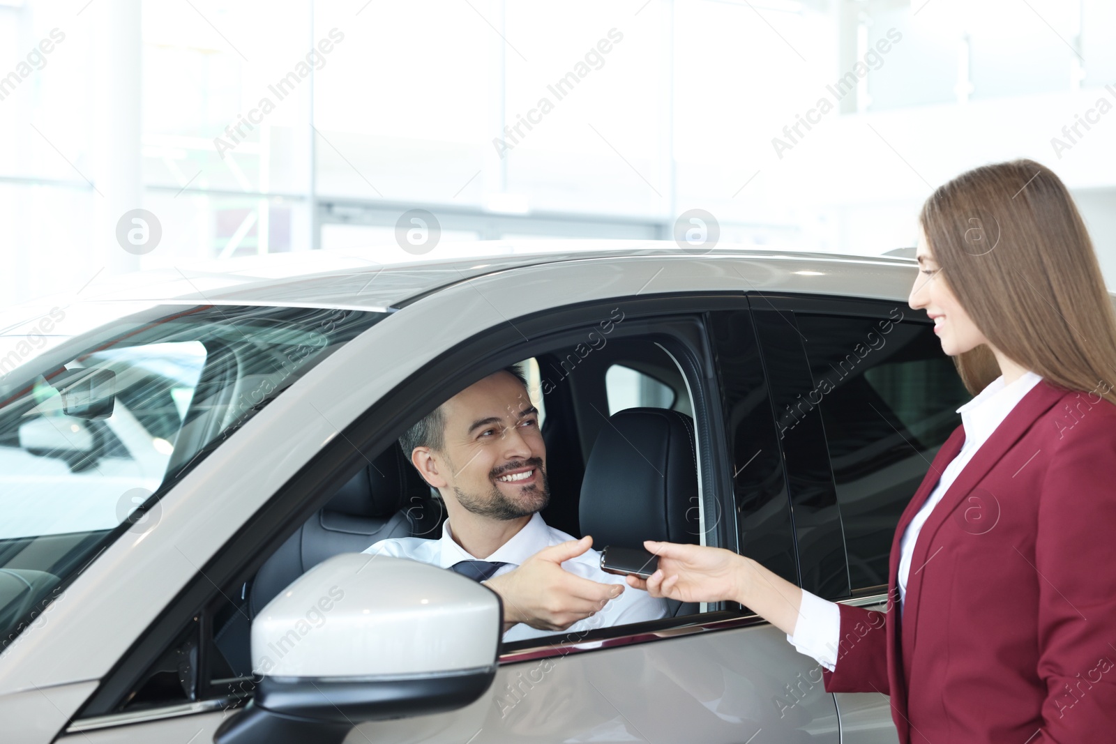 Photo of Happy saleswoman and client inside new silver car in salon