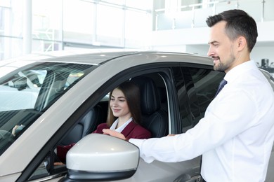 Photo of Happy salesman showing car to client in salon