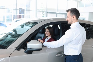 Photo of Happy salesman showing car to client in salon