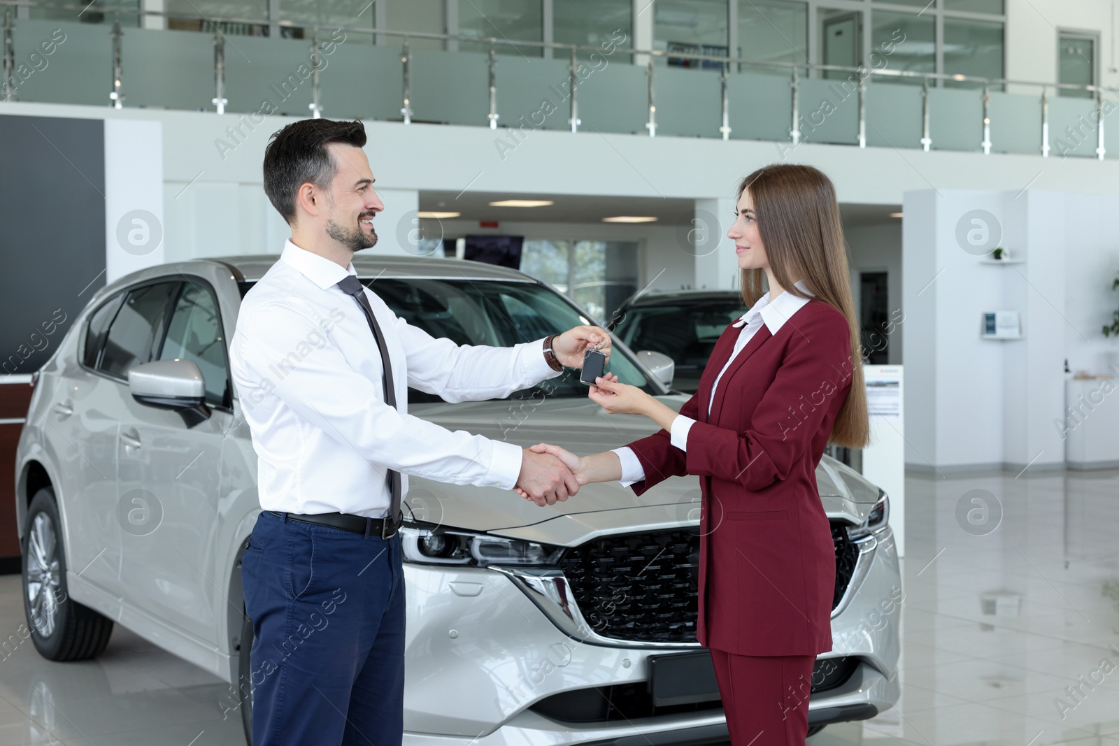 Photo of Salesman giving key to client near new car in salon