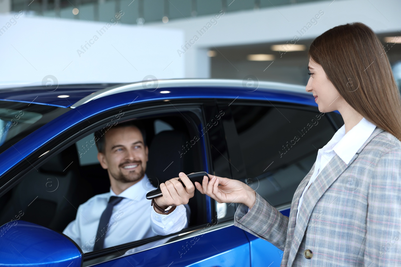 Photo of Saleswoman giving key to client inside new car in salon, selective focus