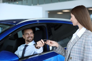 Saleswoman giving key to client inside new car in salon, selective focus