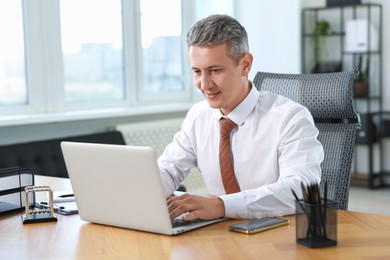 Photo of Middle aged man working with laptop at table in office