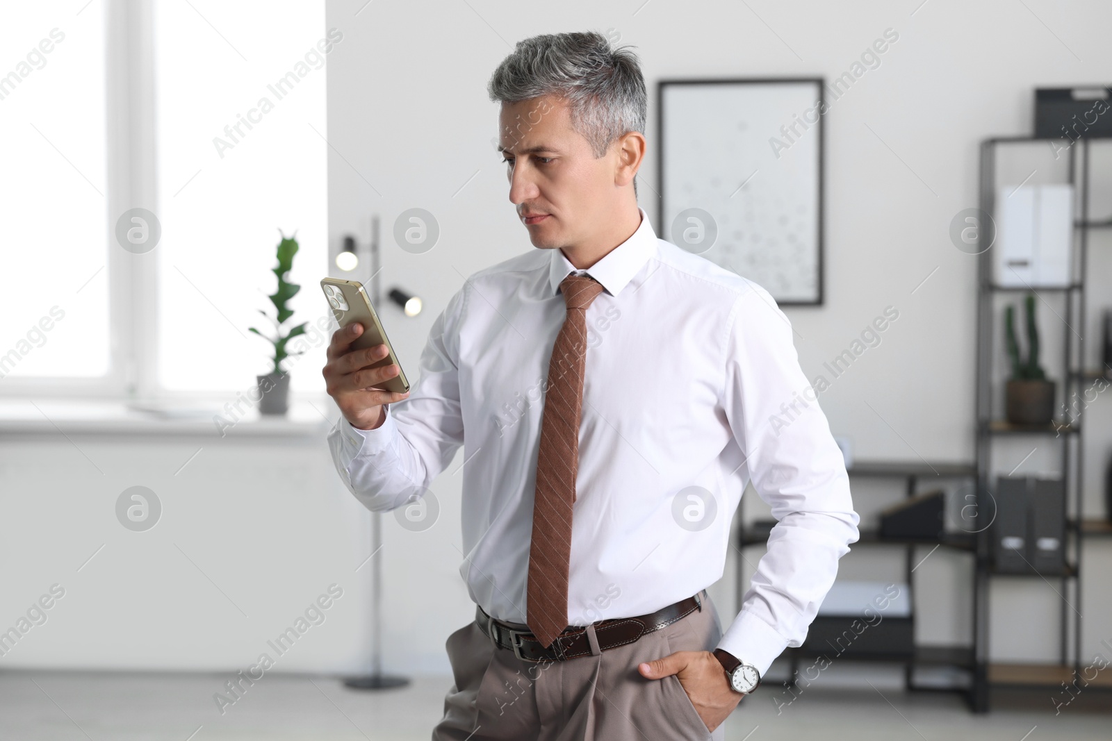 Photo of Middle aged man looking at smartphone in office