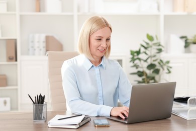 Photo of Smiling middle aged woman working with laptop at table in office