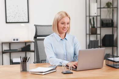 Photo of Smiling middle aged woman working with laptop at table in office