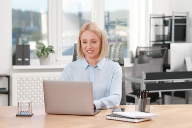 Smiling middle aged woman working with laptop at table in office