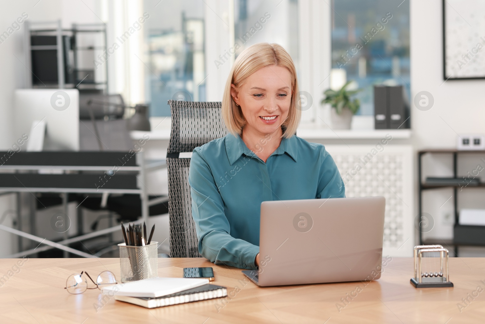 Photo of Smiling middle aged woman working with laptop at table in office