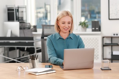 Photo of Smiling middle aged woman working with laptop at table in office