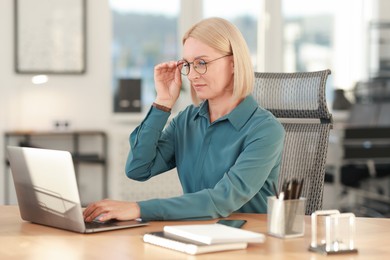 Photo of Middle aged woman working with laptop at table in office