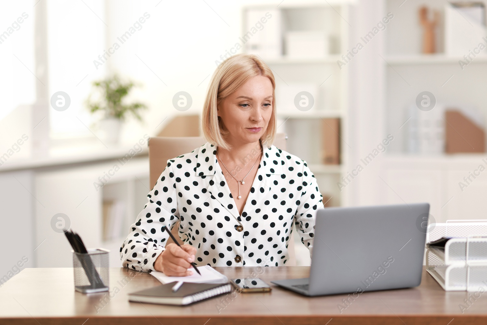 Photo of Middle aged woman working with laptop at table in office