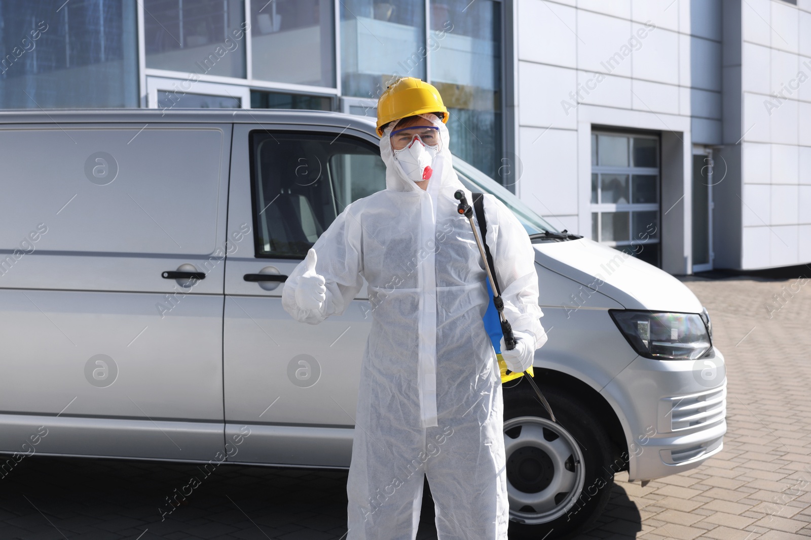 Photo of Pest control worker with spray tank showing thumbs up outdoors