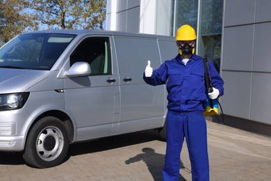 Photo of Pest control worker with spray tank showing thumbs up outdoors