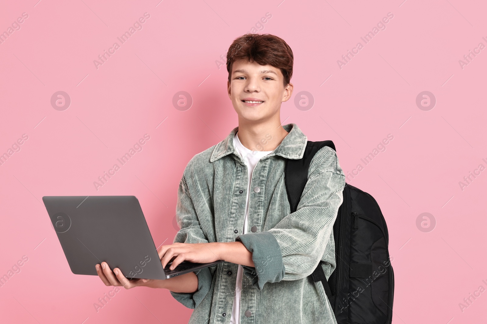 Photo of Happy teenage boy with laptop and backpack on pink background