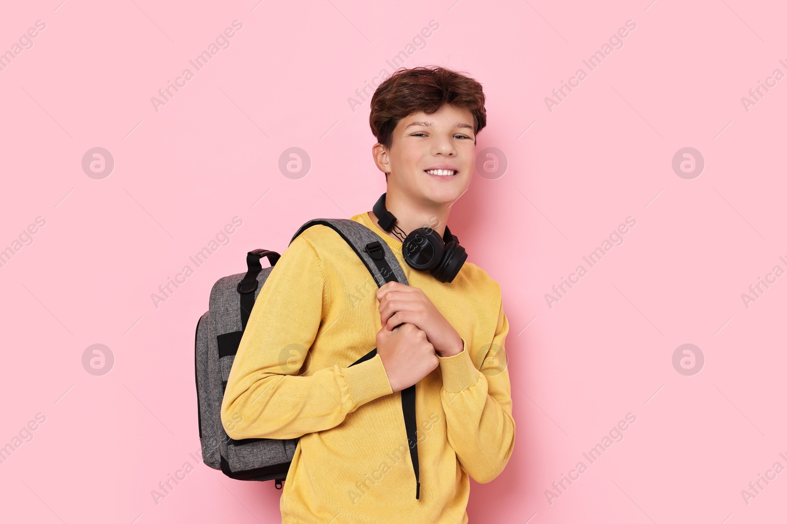 Photo of Happy teenage boy with headphones and backpack on pink background