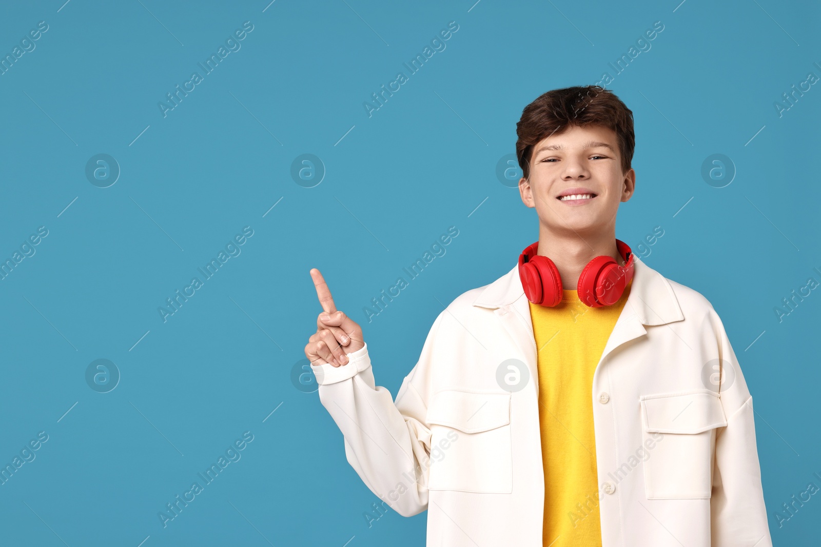 Photo of Happy teenage boy with headphones on light blue background, space for text