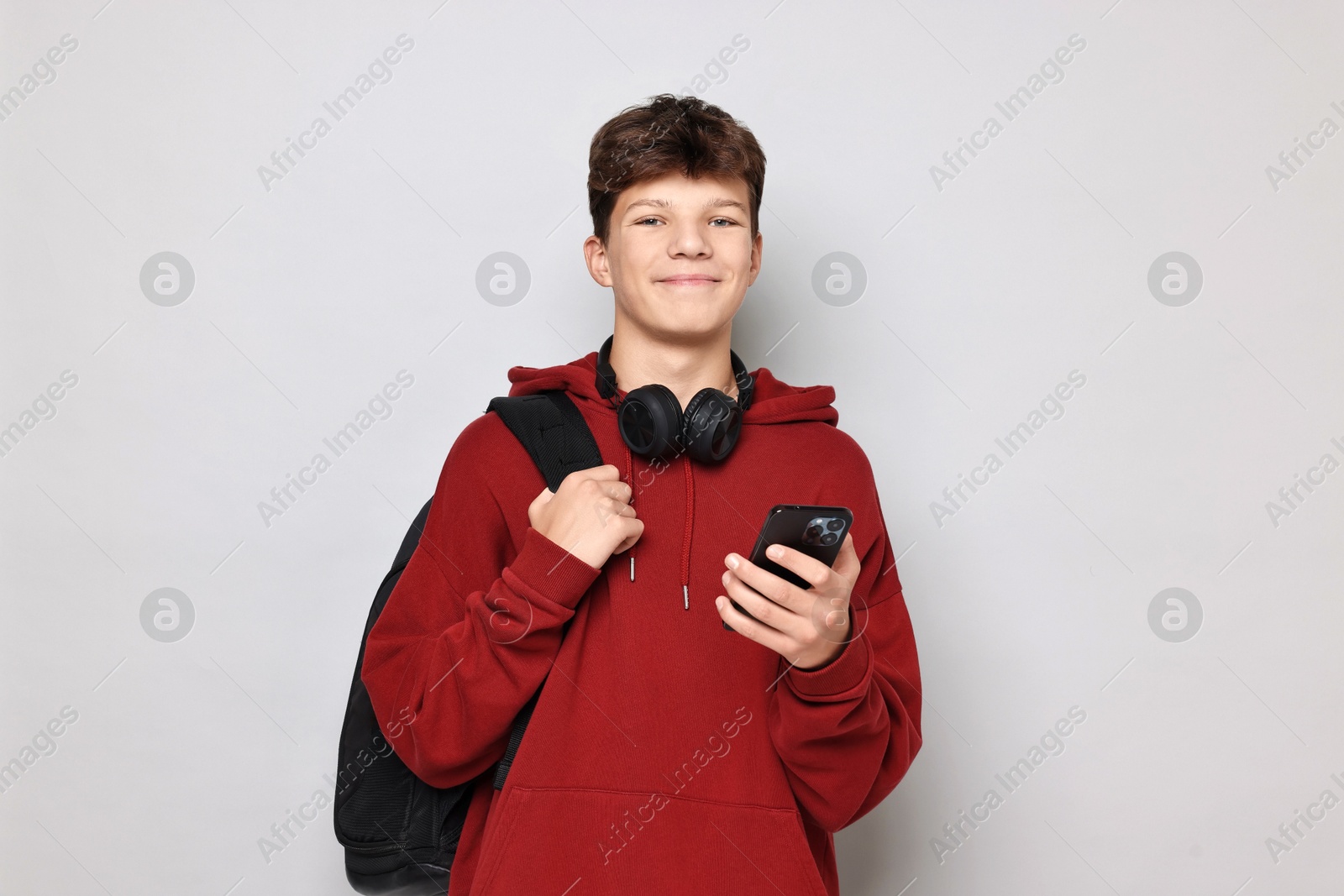 Photo of Teenage boy with headphones, smartphone and backpack on light grey background