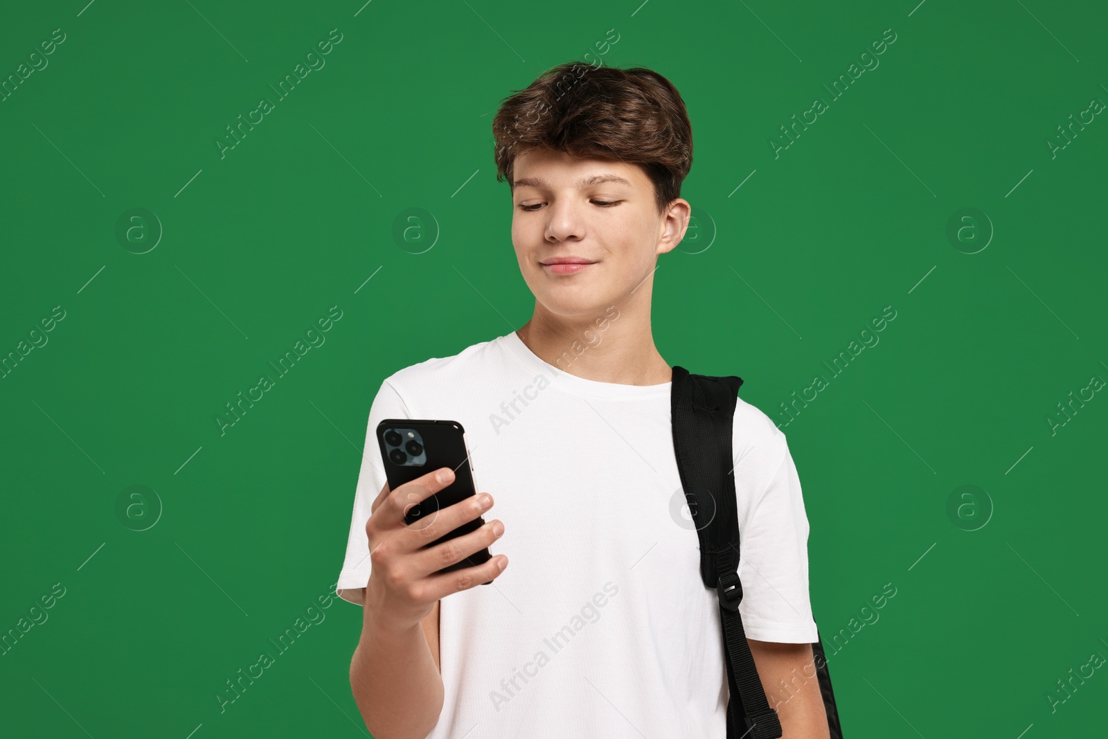 Photo of Teenage boy with smartphone and backpack on green background