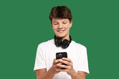 Photo of Teenage boy with headphones and smartphone on green background