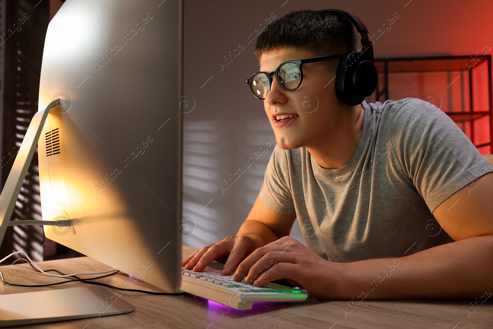 Photo of Young man playing video game with keyboard at wooden table indoors