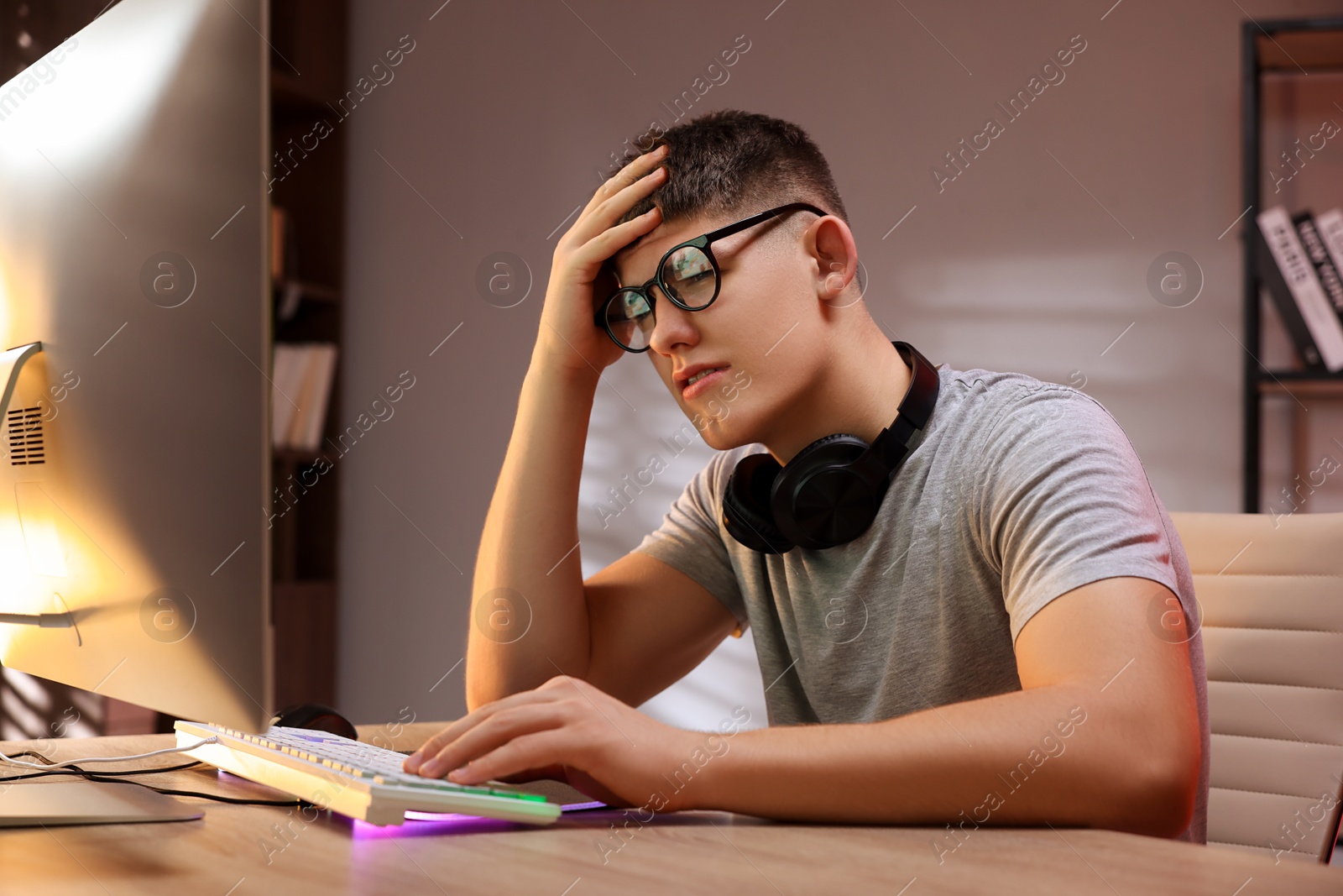 Photo of Young man playing video game with keyboard at wooden table indoors