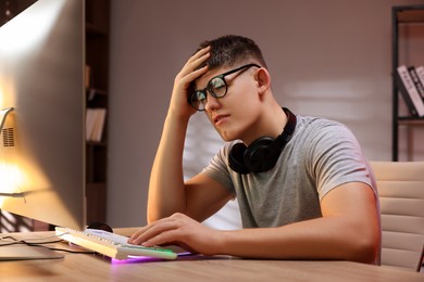 Photo of Young man playing video game with keyboard at wooden table indoors