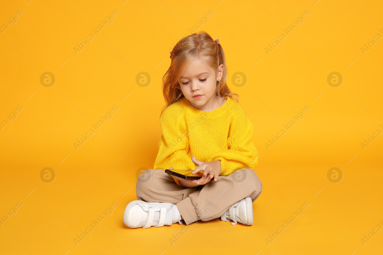 Photo of Cute little girl with smartphone against orange background