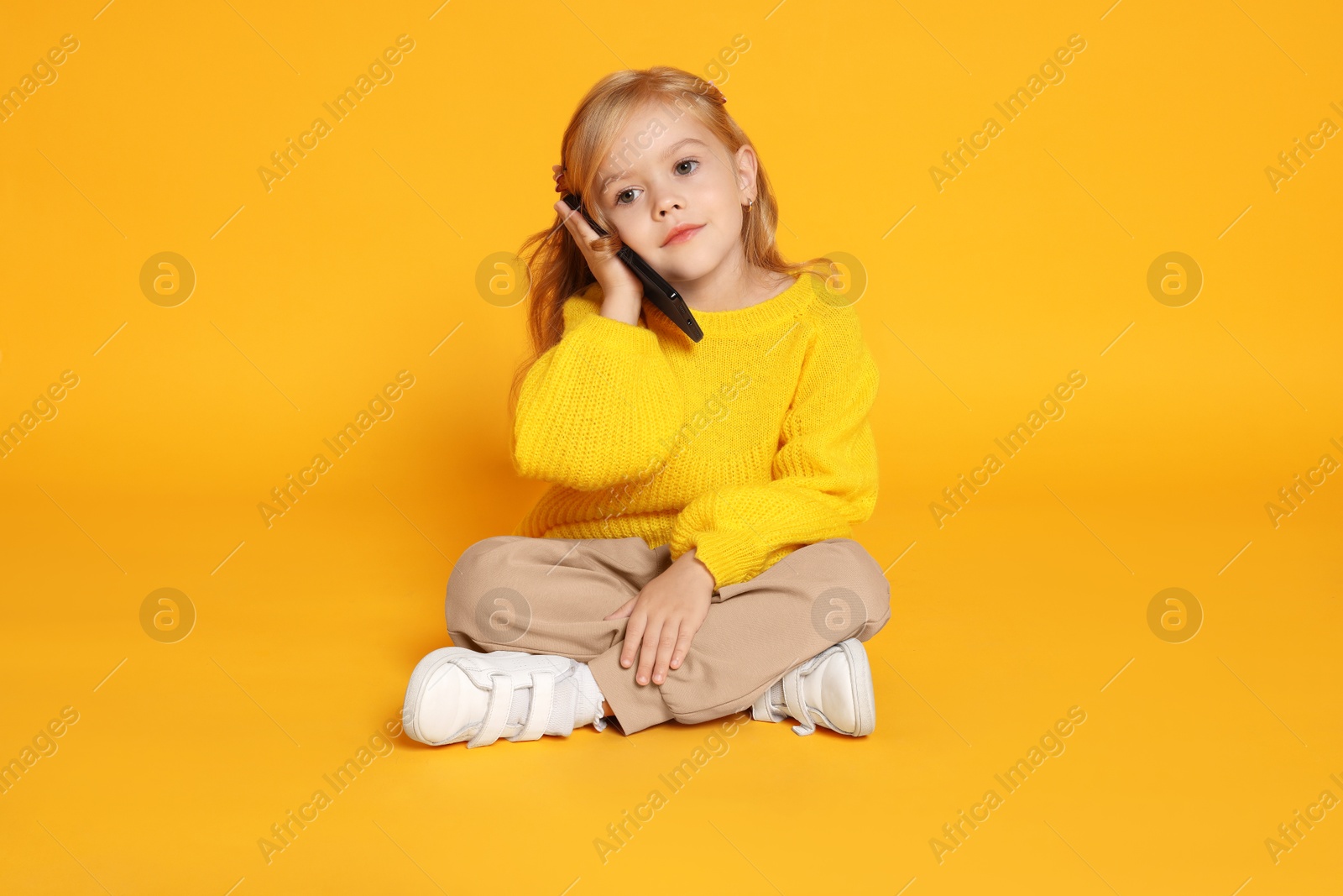 Photo of Cute little girl talking on smartphone against orange background