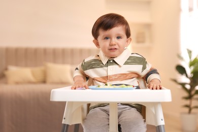 Photo of Cute little baby eating healthy food in high chair at home