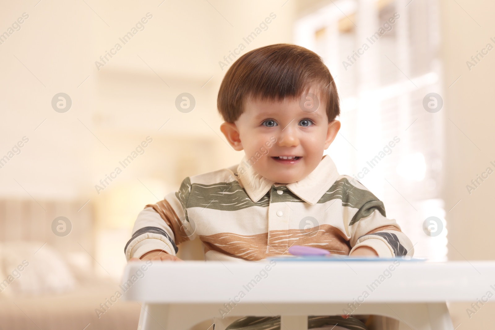 Photo of Cute little baby eating healthy food in high chair at home