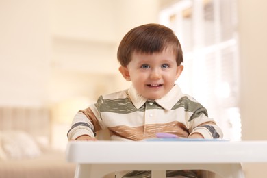 Photo of Cute little baby eating healthy food in high chair at home