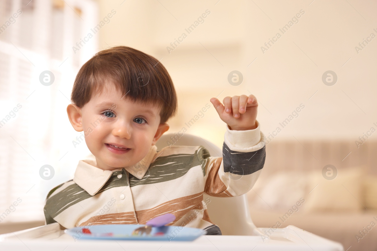 Photo of Cute little baby eating healthy food in high chair at home