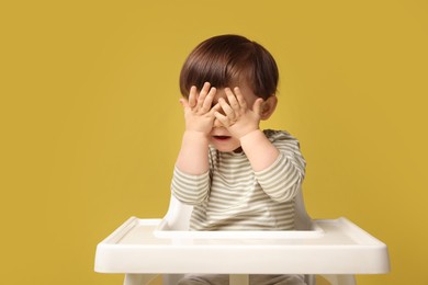 Photo of Cute little kid sitting in high chair on yellow background