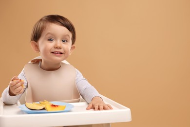 Photo of Healthy baby food. Cute little kid eating fruits in high chair on beige background, space for text