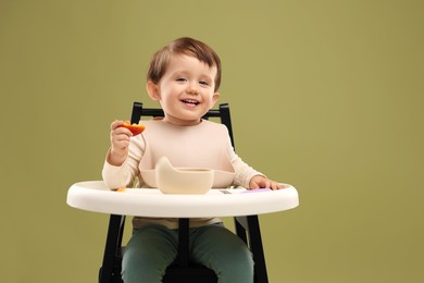 Photo of Cute little baby eating healthy food from bowl in high chair on olive background